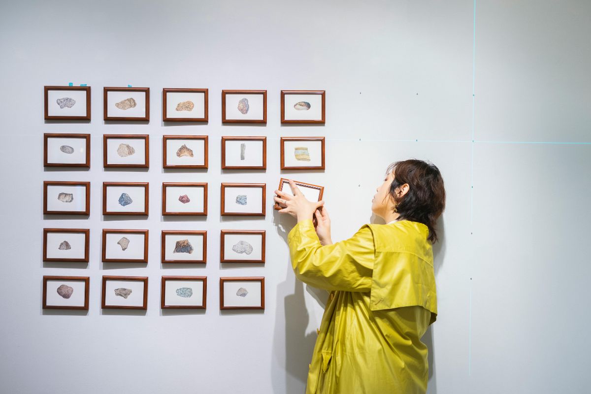 Dame en manteau jaune qui installe des tableaux au mur